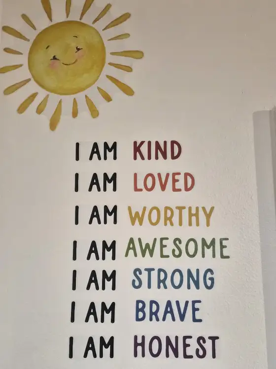 A wall painted with I am kind, I am loved, I am worthy and more, beneath a smiling sun