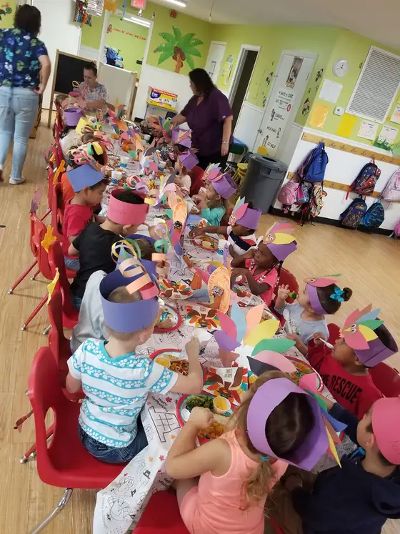 Children in paper visors working along a long craft table